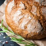 Loaf of Rosemary Bread with salt and pepper and a sprig of rosemary on paper.