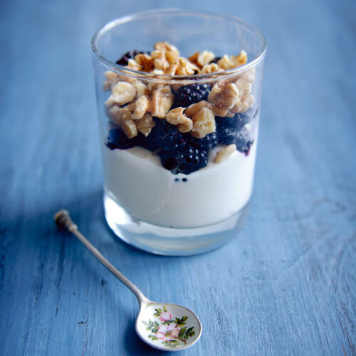 A parfait with granola and a metal spoon beside it.
