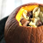 A closeup of a roasted pumpkin that is stuffed with pasta.