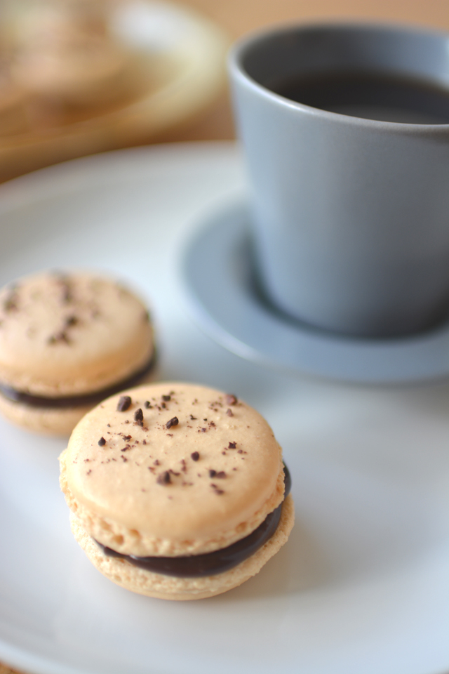 close-up image featuring two delectable chocolate coffee macarons beside a steaming cup of coffee