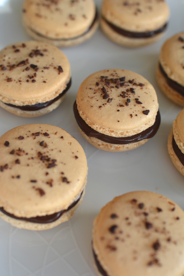 top view image of a batch of chocolate coffee macarons, garnished with chocolate chunks and the filling is generously overflowing