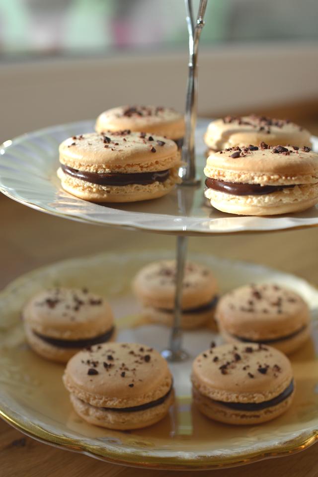 close-up image of a two-tiered cake plate featuring beautifully arranged chocolate coffee macarons