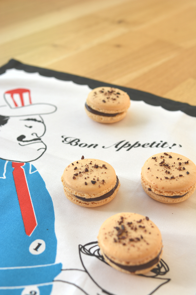 flatlay view of four chocolate coffee macarons arranged on a tea towel, each topped with decadent chocolate chunks
