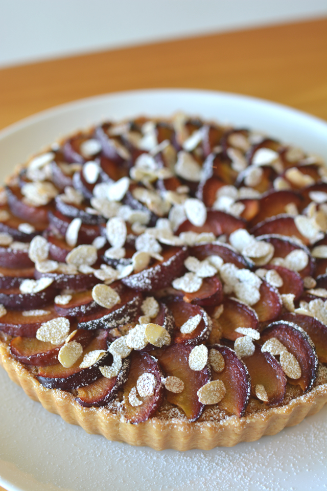close up image of a single plum and almond tart topped with flaked almonds