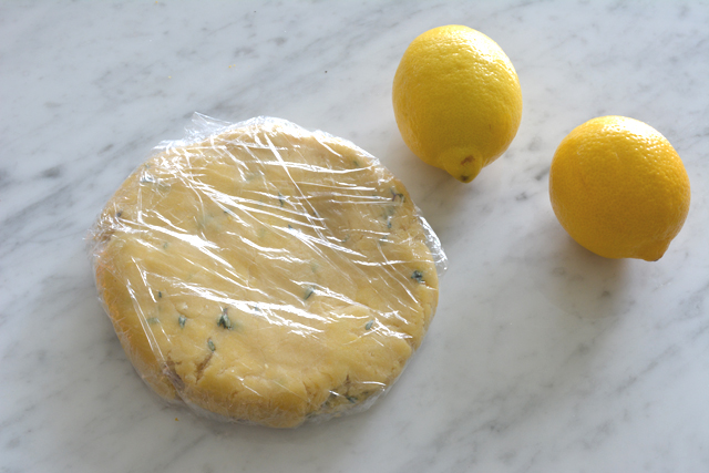 image of cookie dough resting in cling wrap with two fresh lemons on the side