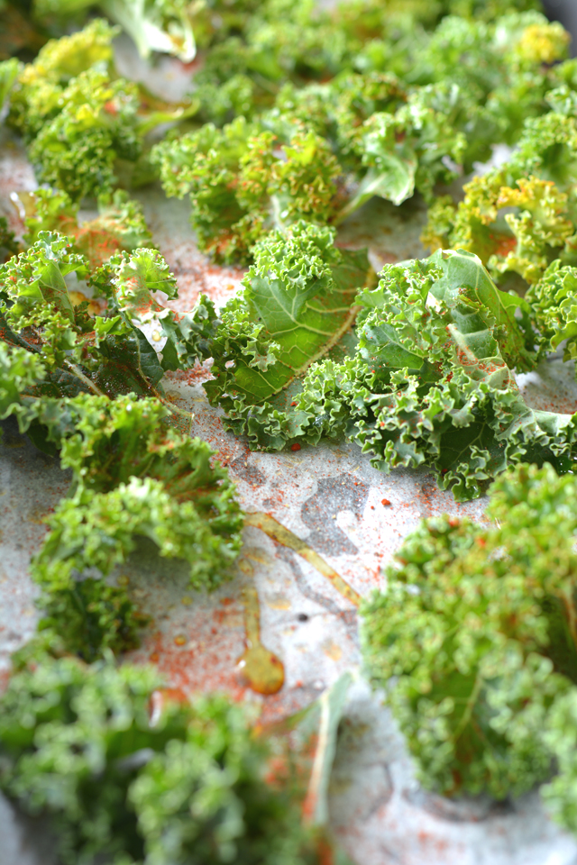 a baking tray filled with fresh kale leaves, evenly coated with seasonings