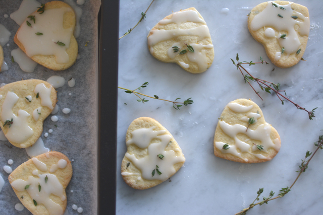 top down image of seven heart-shaped Lemon Thyme Mint Cookies, delicately drizzled with icing and adorned with fresh thyme leaves