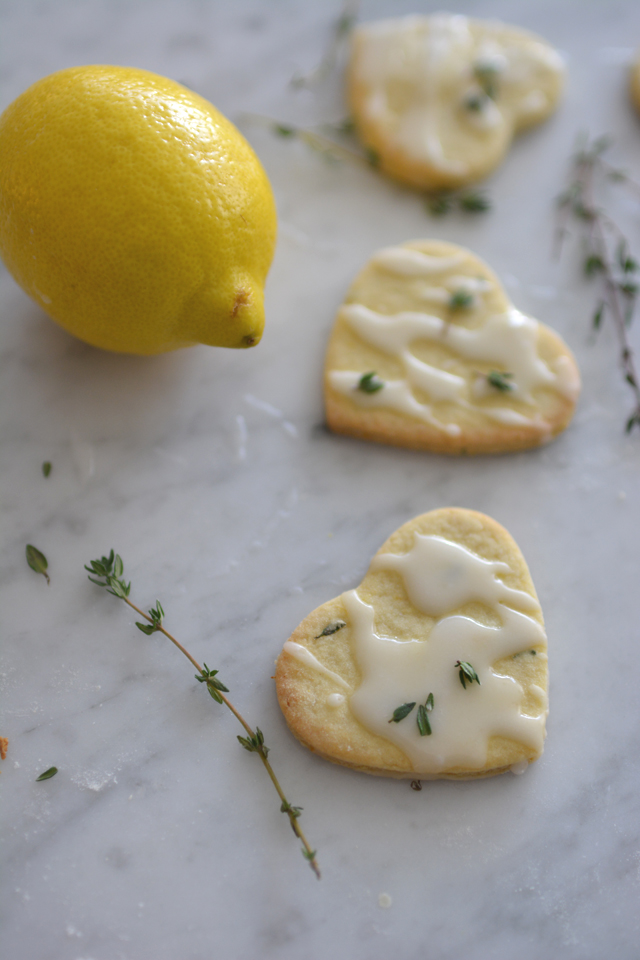 three Lemon Thyme Mint Cookies arranged in a row with a drizzle of icing, accompanied by a fresh lemon on the side