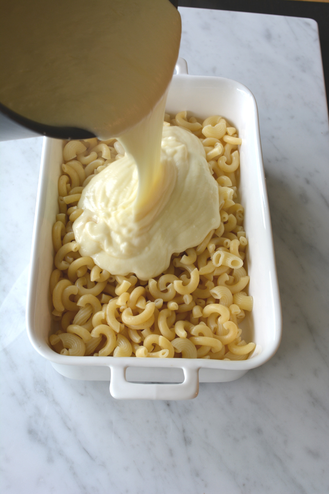top-down view of creamy cheese sauce poured over cooked macaroni in a rectangular dish