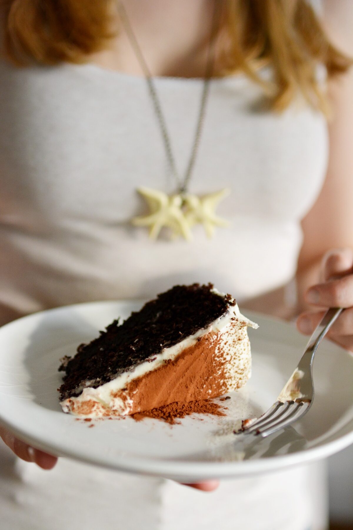 close-up photo of a woman holding a plate with a slice of chocolate Guinness cake on it, along with a fork