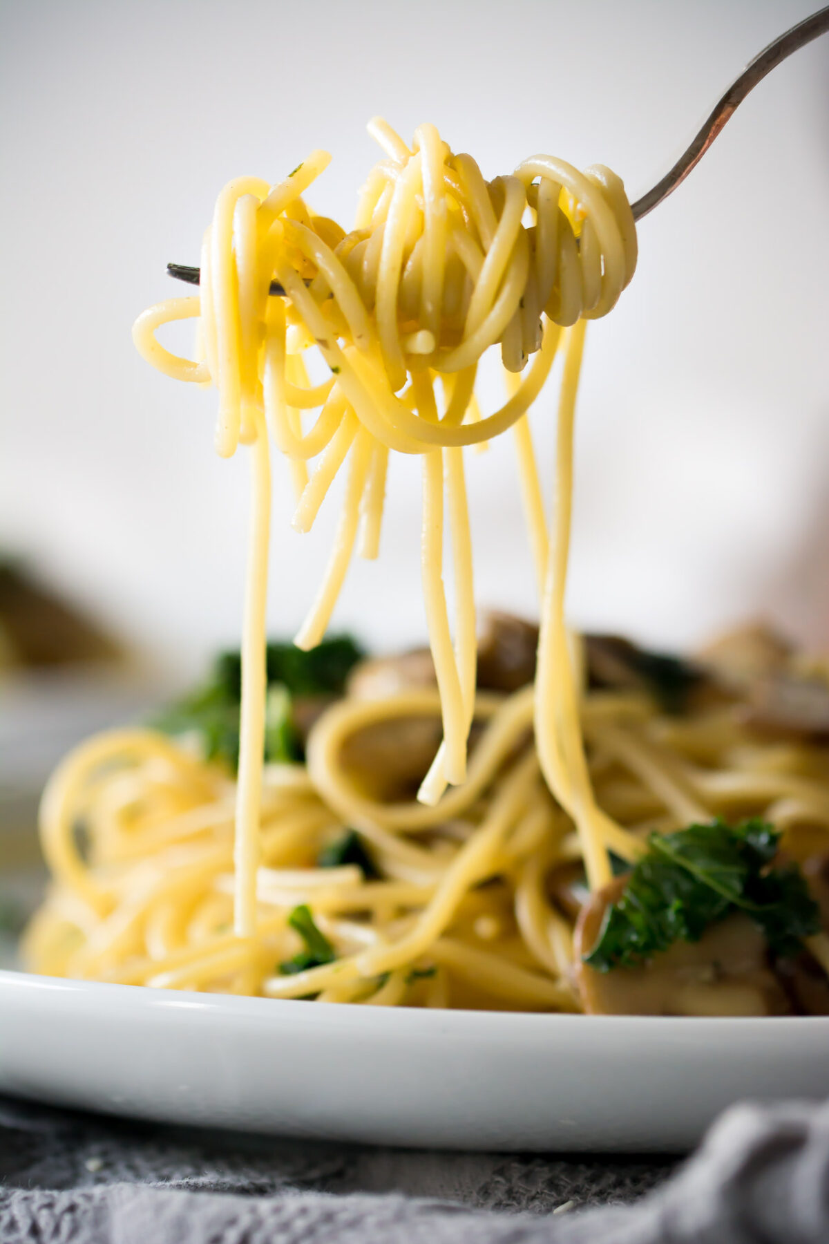 Freshly made spaghetti pasta with kale and mushrooms on a white plate and cloth napkin.