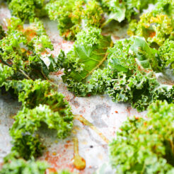 a baking tray filled with fresh kale leaves, evenly coated with seasonings