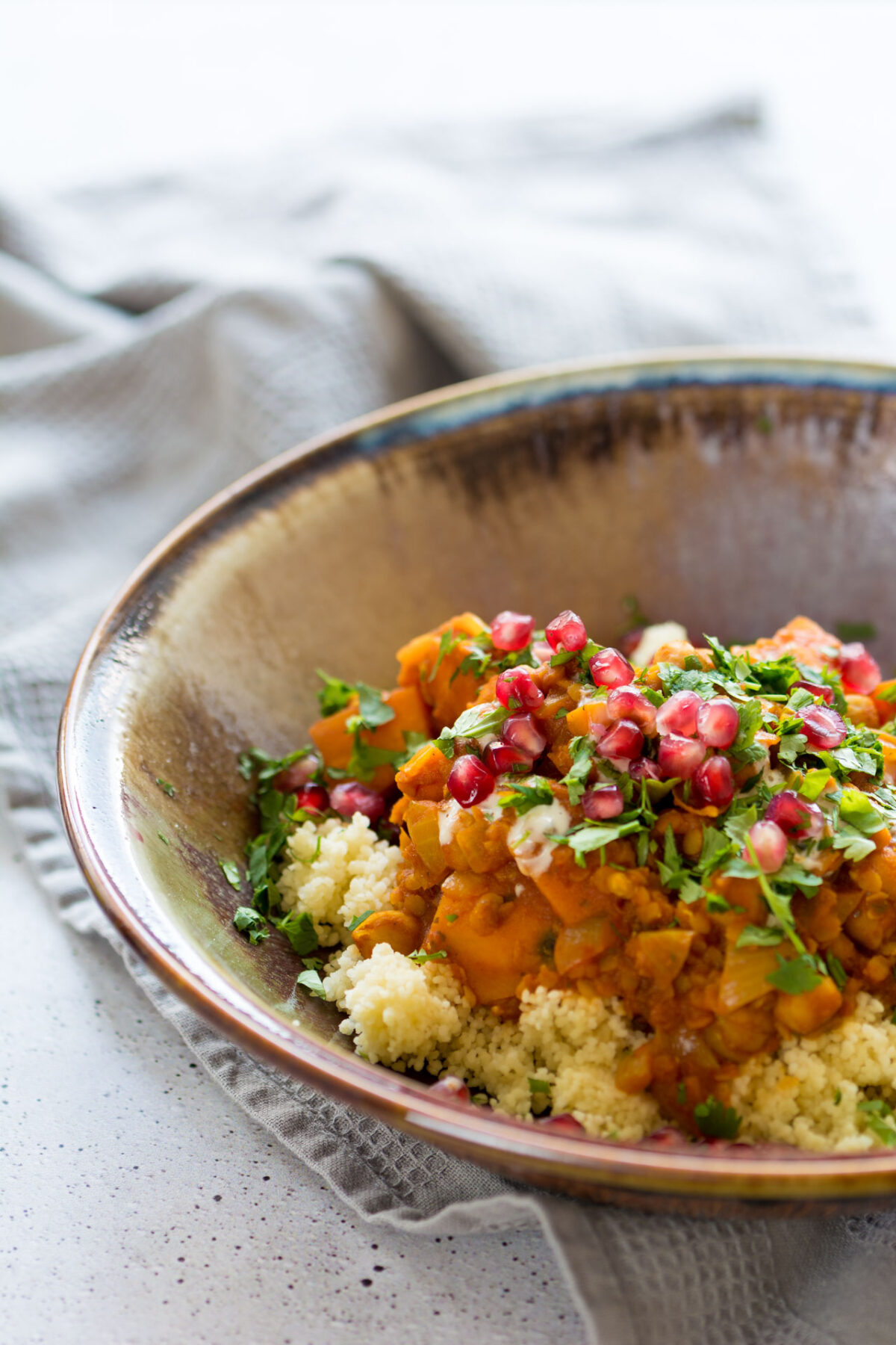 Sweet Potato and Chickpea Moroccan Style Stew in a tan glazed dish on top of a cloth napkin on a white speckled tabletop.