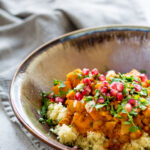 Sweet Potato and Chickpea Moroccan Style Stew in a tan glazed dish on top of a cloth napkin on a white speckled tabletop.