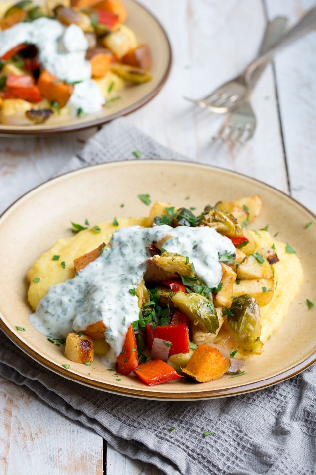 close up image of a colorful roasted vegetables, creamy polenta, and zesty herby yogurt sauce on a plate