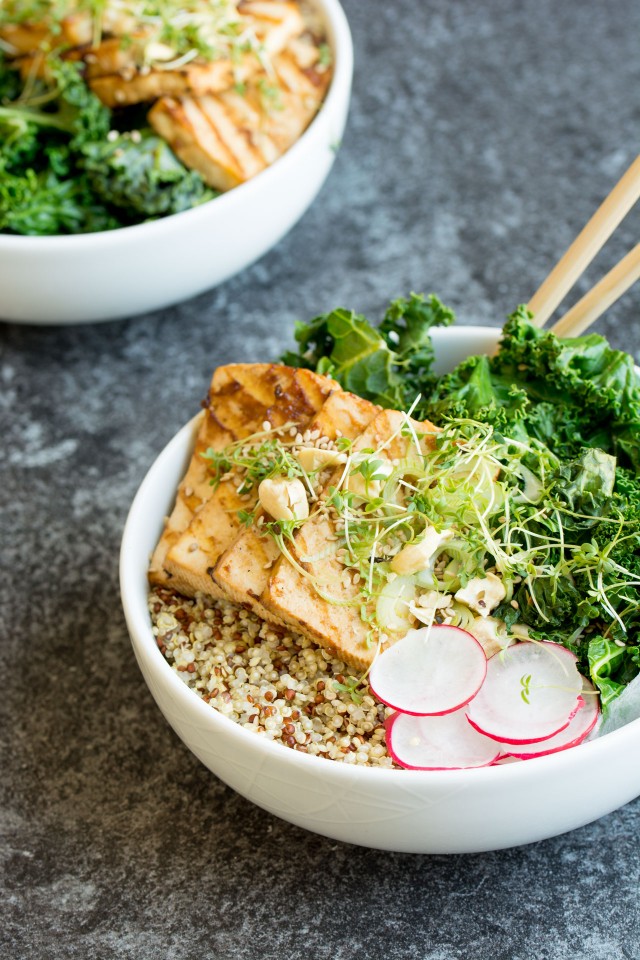 close up image of a teriyaki tofu in a bowl with kale and nuts on top