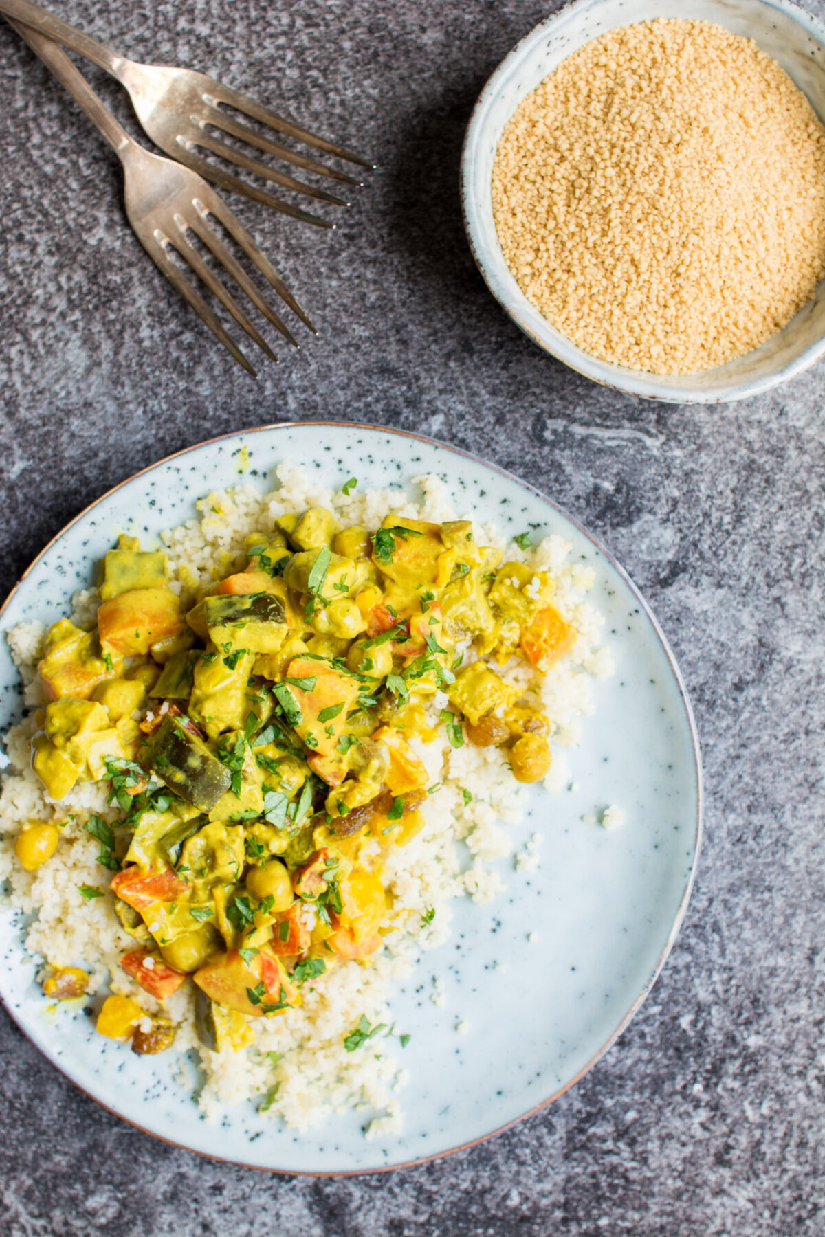 Vegetable curry with turmeric on a white place over a gray background with two forks.