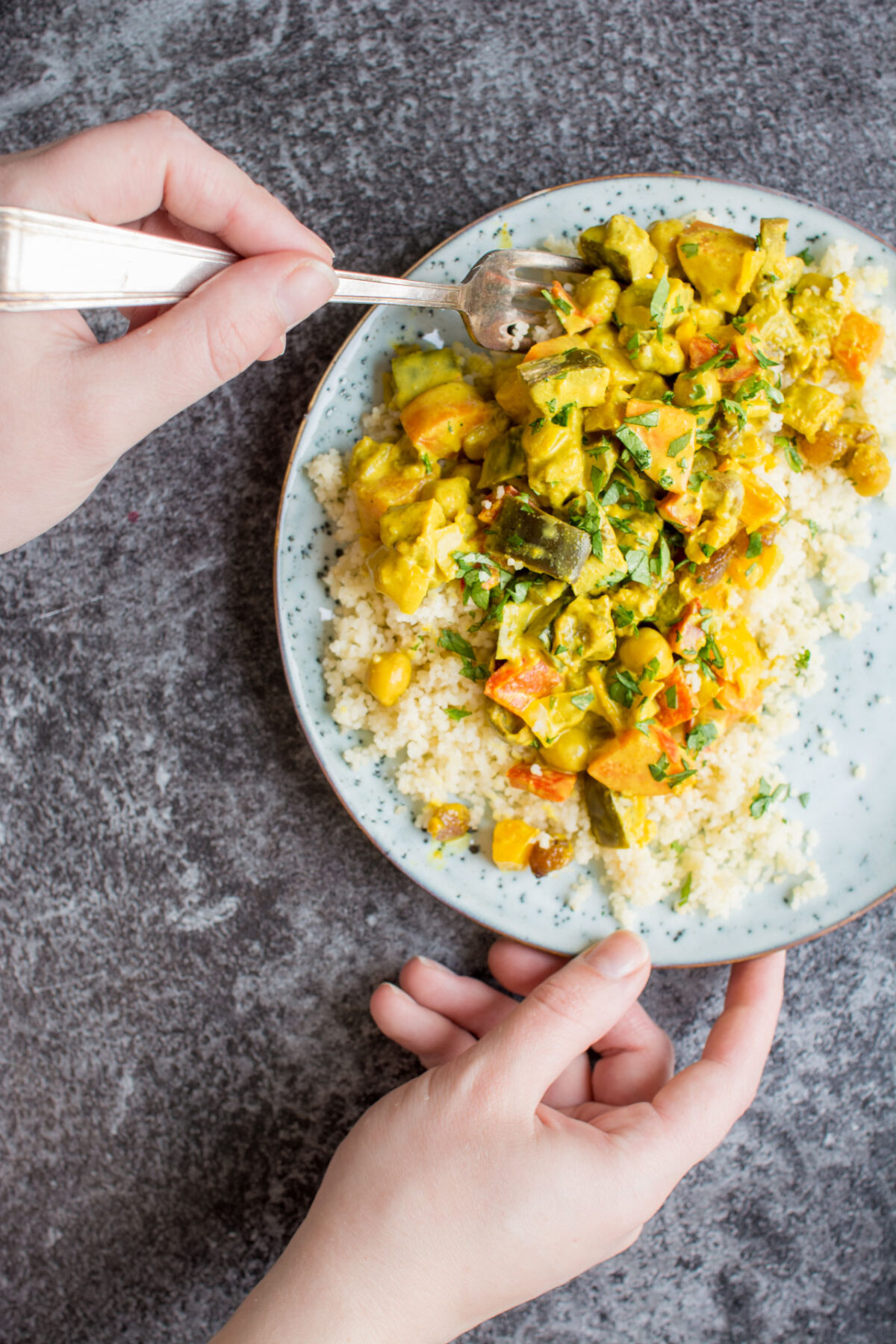 Vegetable curry with turmeric on a white place over a gray background with a woman's hand using a fork.