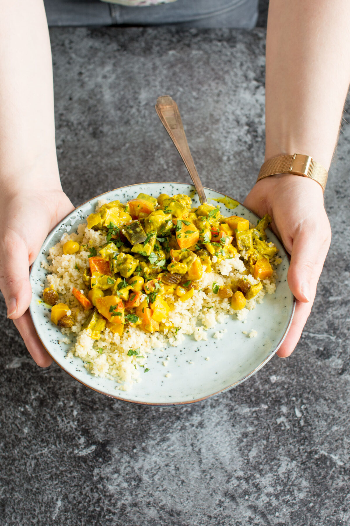 A woman's hands holding a plate of vegetable curry with turmeric.