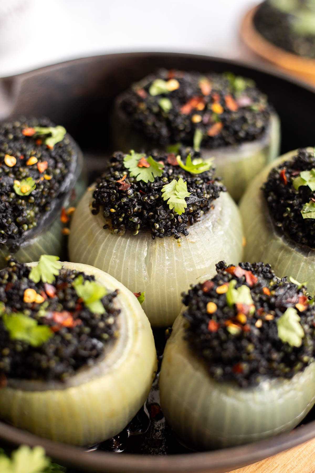 Onions stuffed with curried black quinoa and cilantro garnish in a cast iron pan.