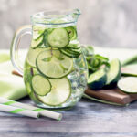 A glass pitcher filled with cucumber water, flavored with lime and mint.