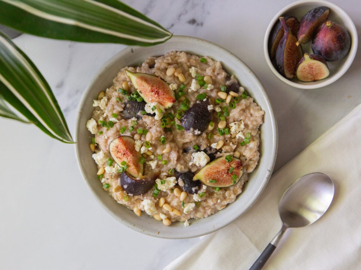 A white bowl filled with savory oatmeal with figs and feta and a napkin with a spoon with a small bowl filled with figs.