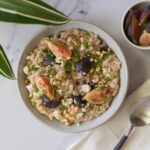 A white bowl filled with savory oatmeal with figs and feta and a napkin with a spoon with a small bowl filled with figs.